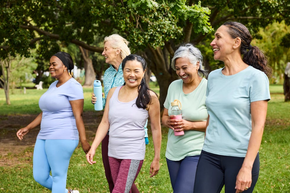 happy group of women talking with each other in park. multiracial female friends are walking together after yoga routine. they are wearing sports clothing.