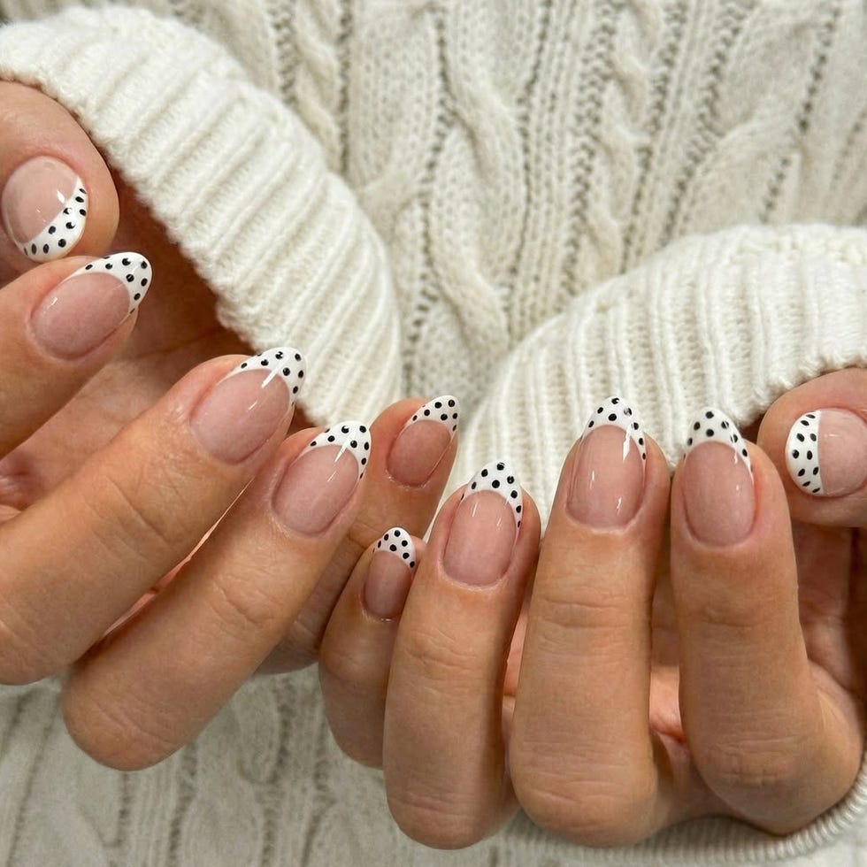 Nail art featuring white tips with black polka dots.