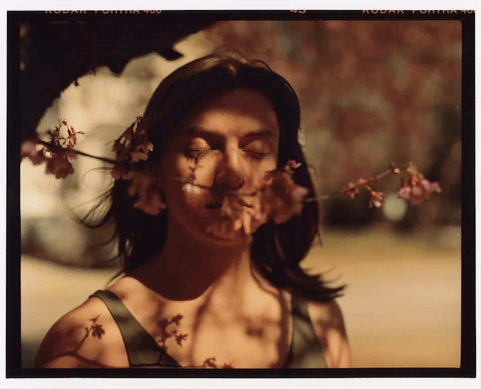 Austen stands outdoors with eyes closed as flowering branches frame her face.