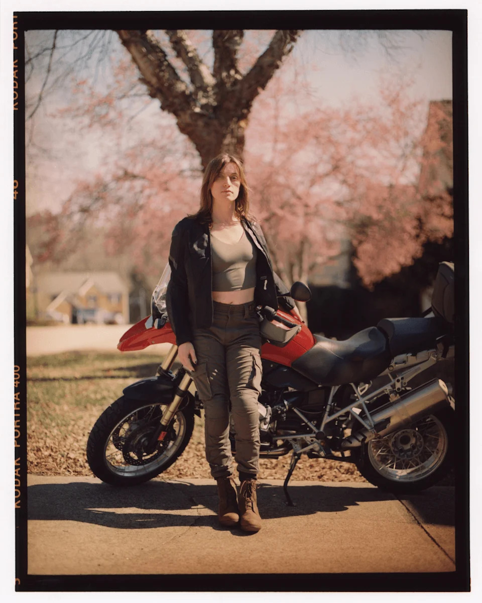 Austen stands in front of a red motorcycle on a quiet residential street.