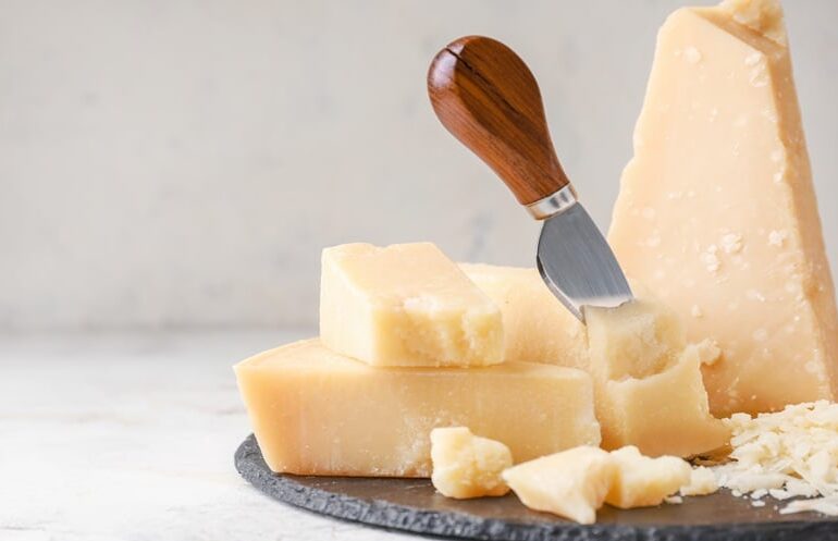 Close up of Parmesan cheese wedges and shavings on a serving board with a cheese knife.