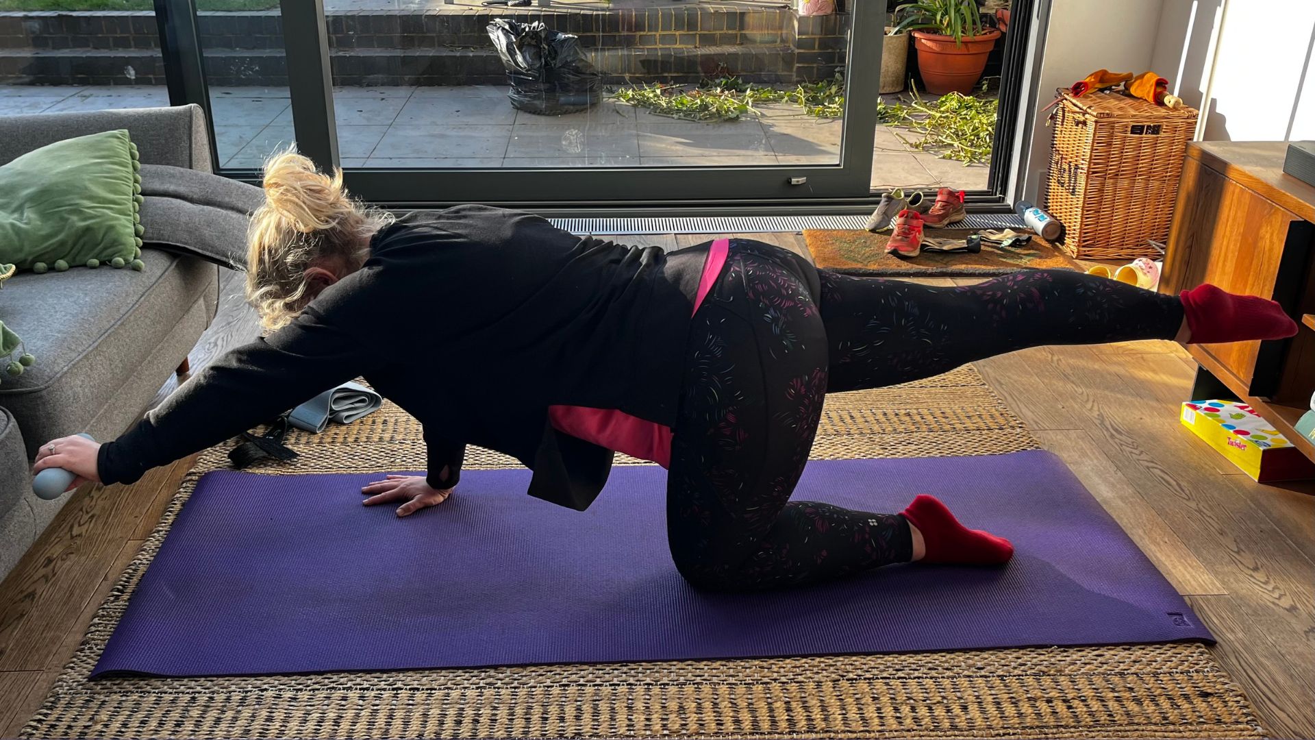 Kat Storr doing 10 minutes of Pilates every day on a yoga mat holding hand weight in bird-dog exercise