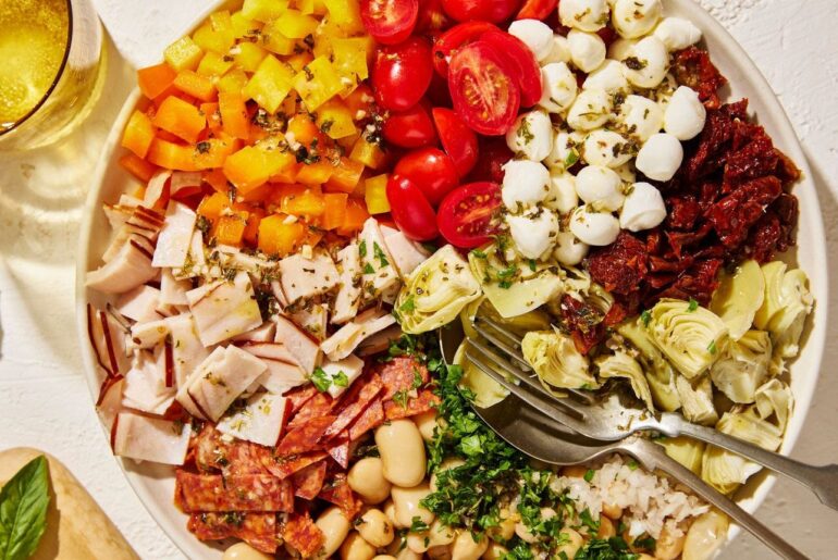 Bowl of ingredients in a pie chart arrangement, including cherry tomatoes, mozzarella balls, sundried tomatoes, artichokes, white beans, pepperoni, deli meat and chopped orange and yellow peppers