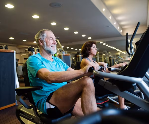 older man, woman on bikes at gym