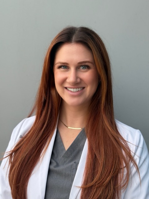 A female dentist wearing a lab coat poses for a headshot.