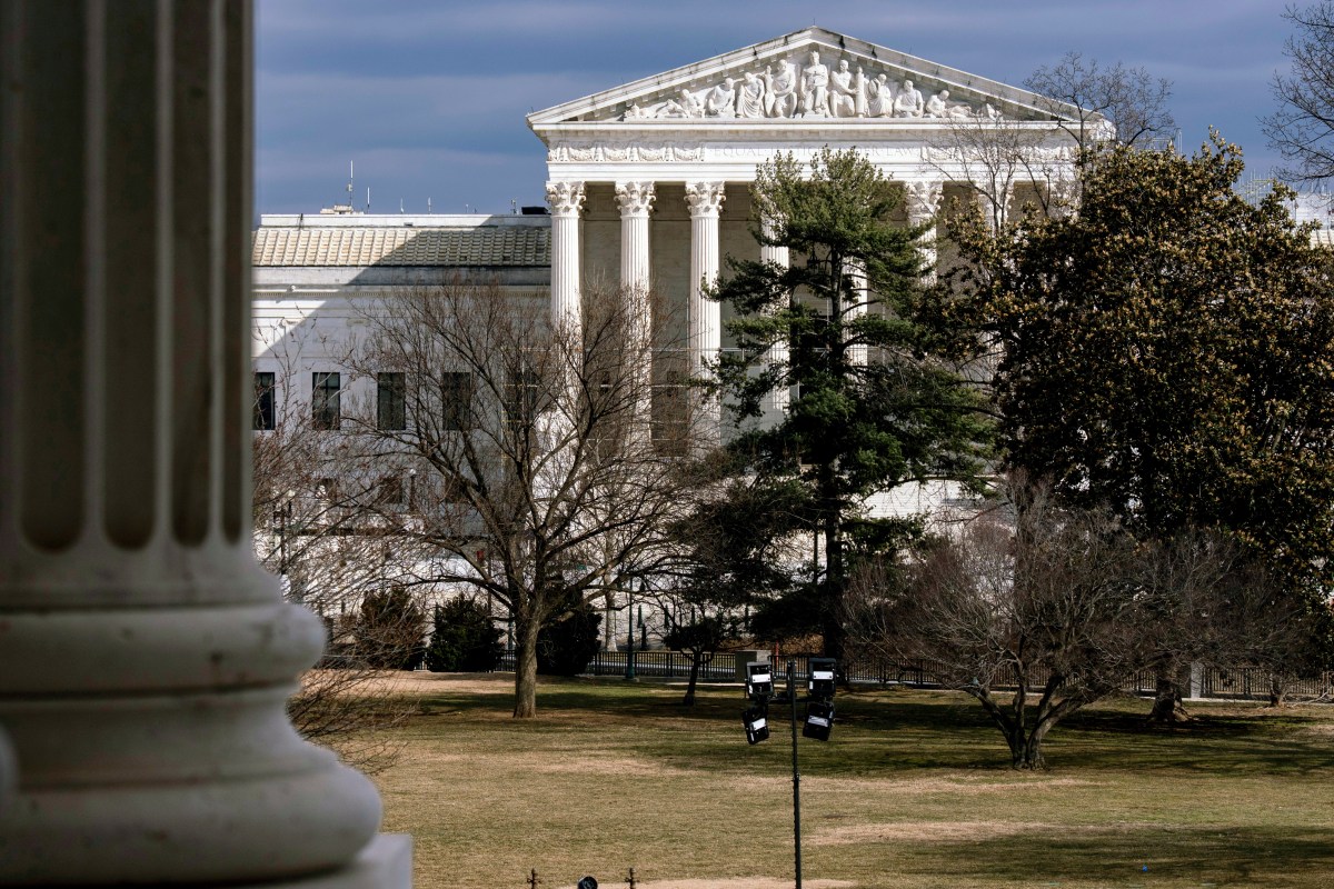 The exterior of the United States Supreme Court building is seen behind trees and a lawn on a cloudy day.