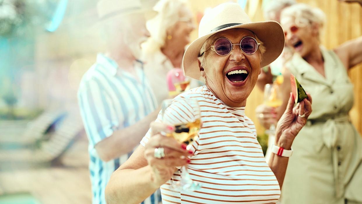 Carefree mature woman having fun with her friends during a summer party by the pool in the backyard and looking at camera.