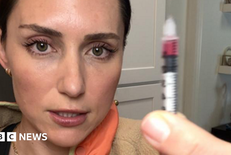 Katie, a woman with brown hair in a ponytail is holding up a syringe and injecting the peptide GHK-Cu into her bum cheek