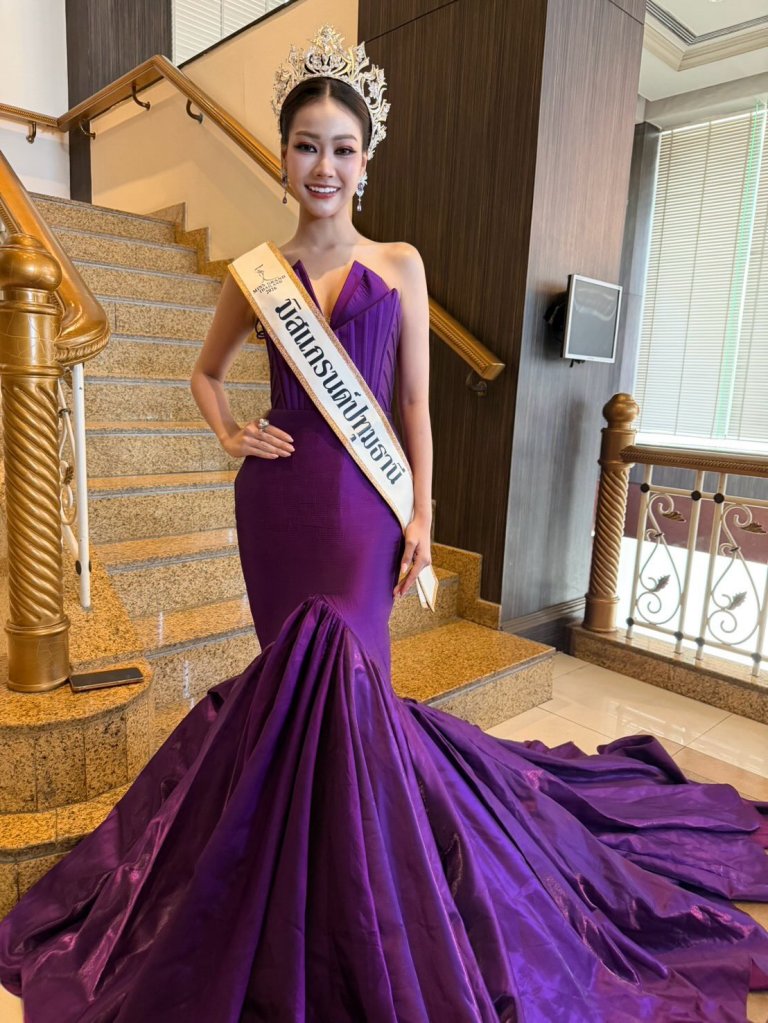 A smiling woman wearing a purple evening gown, tiara, and a sash on a staircase.