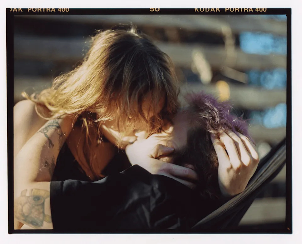 Vali and Mad embrace and kiss while seated together outside.