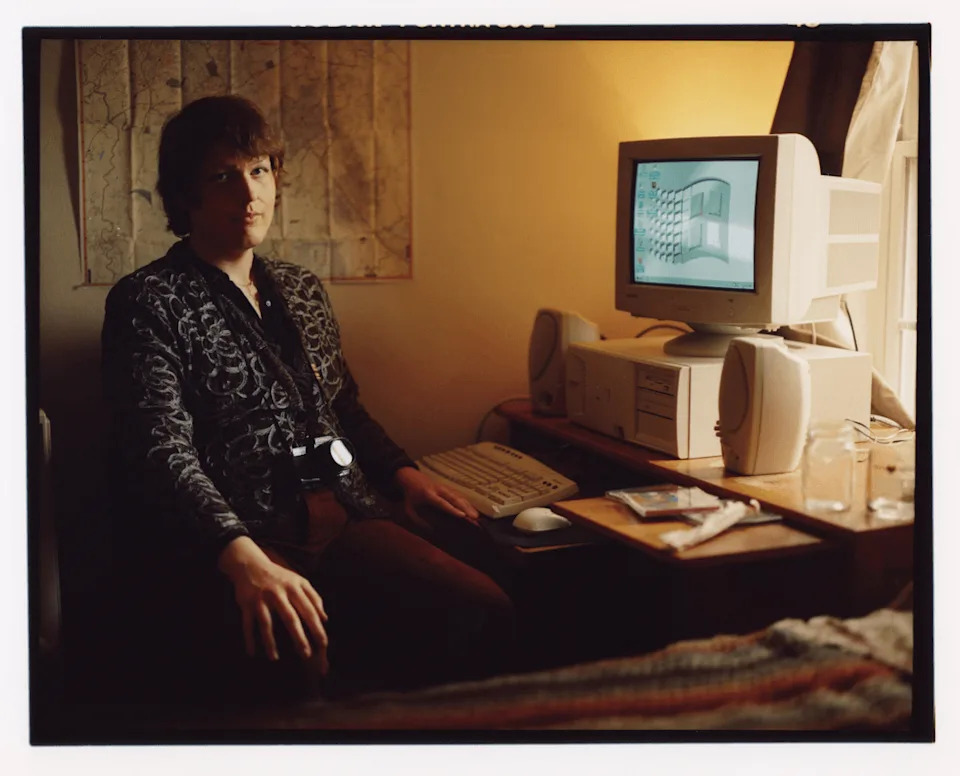 Bailey sits at a desk beside a computer in a softly lit bedroom.