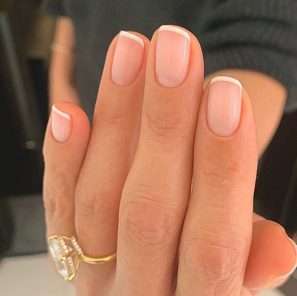 Close-up of manicured nails with french tips and a gold ring.