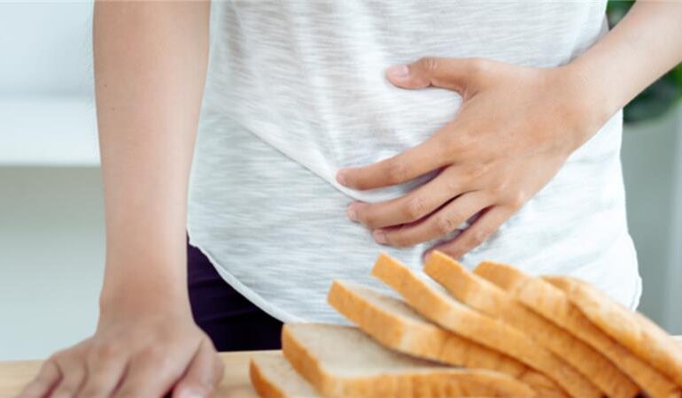 A person holds their stomach. A loaf of bread sits on a counter.