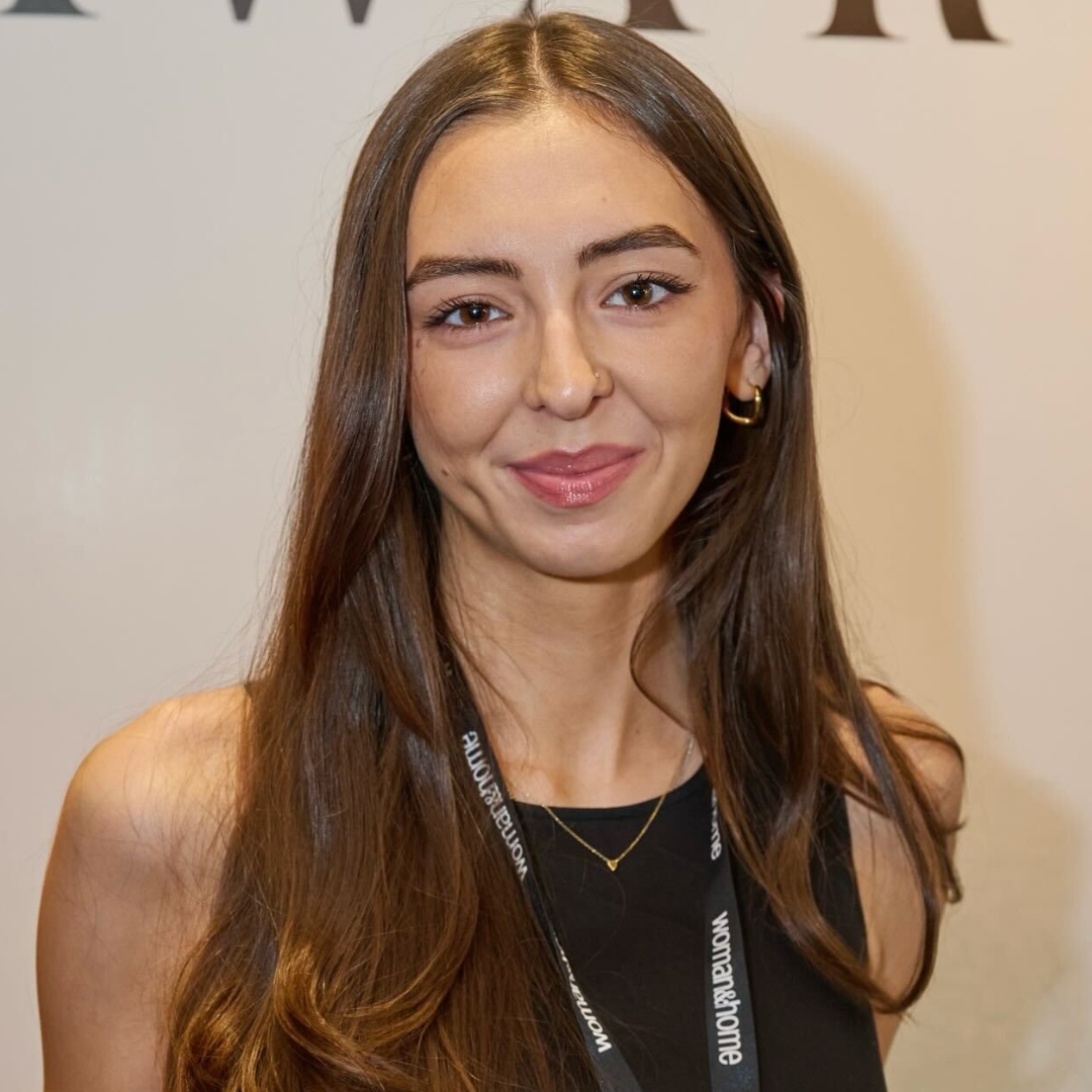 Image of Sennen Prickett smiling with long brunette hair, wearing a black dress and woman&home lanyard
