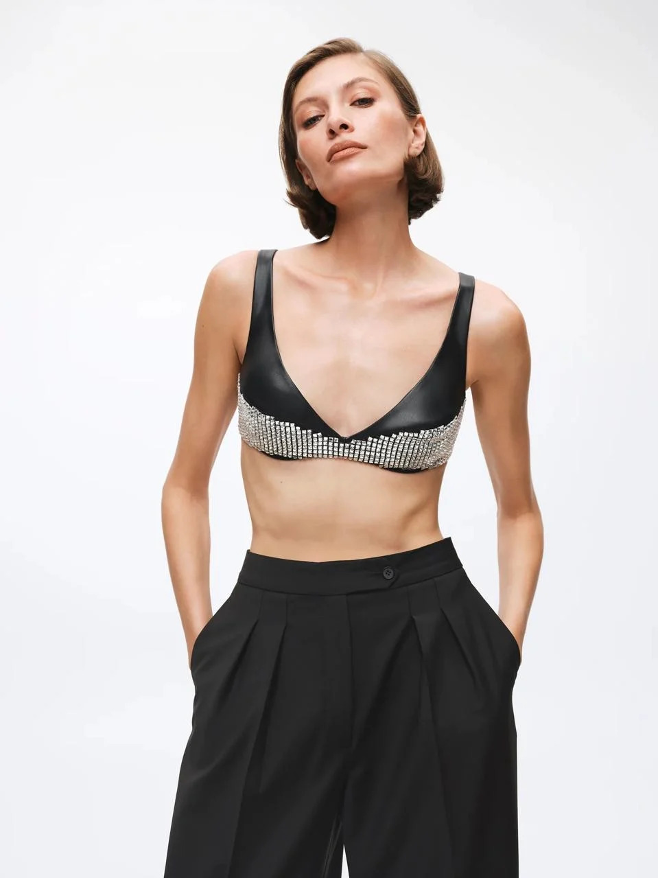 A model wears a cropped leather top with a crystal band across the bust.