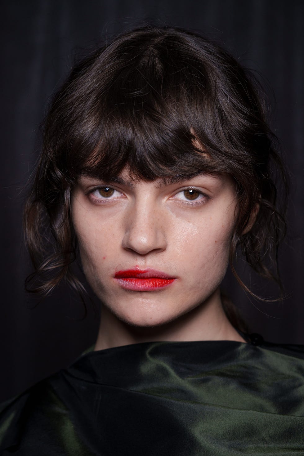 Person with obscured face wearing a black garment against a dark background.