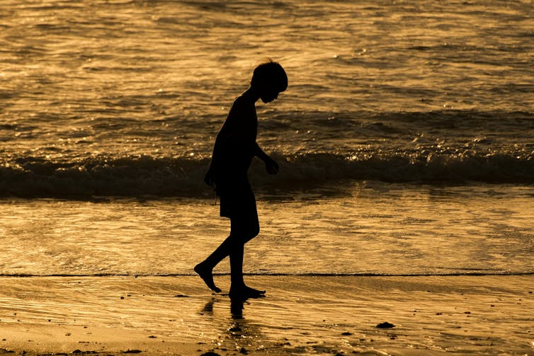 Silhouette of child walking along the waterline of a beach