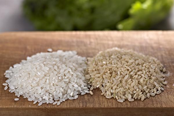 Close-up of two mounds of rice on a wood board, white rice on the left and brown rice on the right.