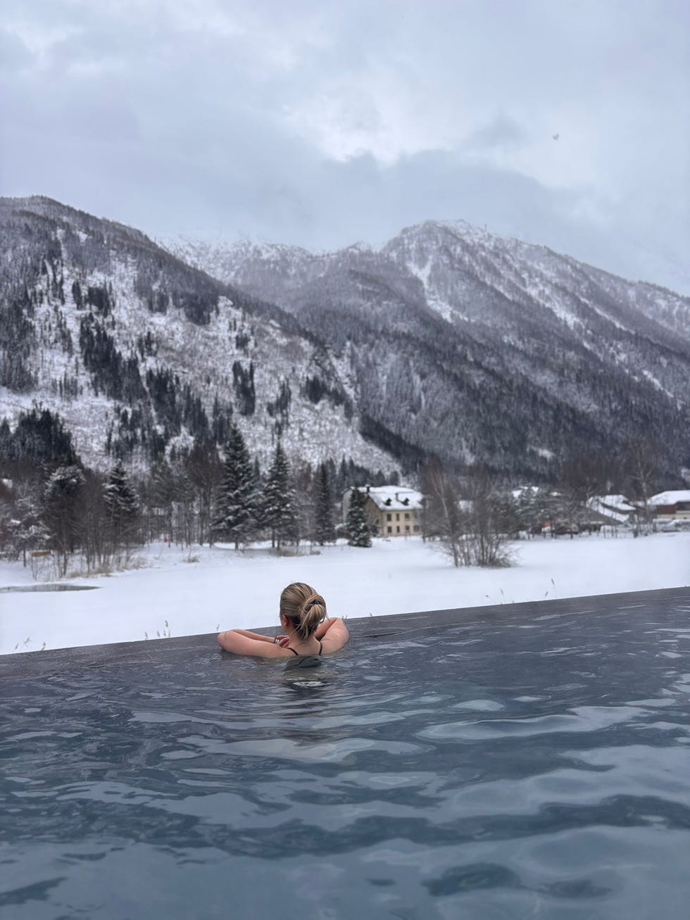 woman relaxing in an infinity pool with snowy mountains and a house in the background girl powder retreat review