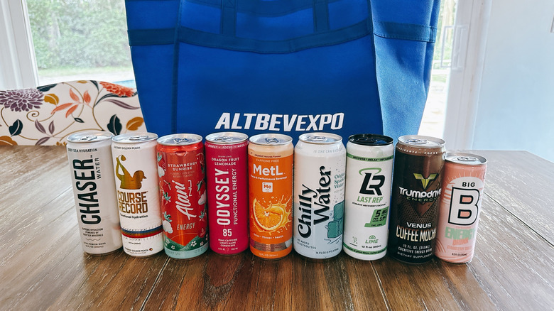 Mix of energy drinks on wooden table in front of a blue bag from the Alt Bev Expo