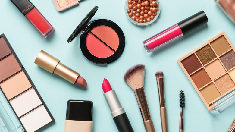 Various eyeshadows, lipsticks, and other beauty products spread out on a teal surface.