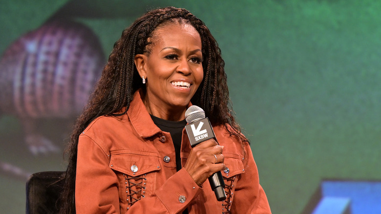 Michelle Obama holds microphone wearing orange jacket