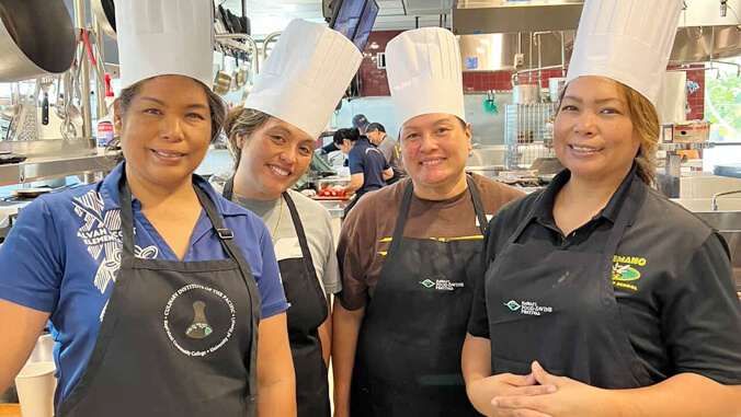 Four smiling people in chef hats and aprons