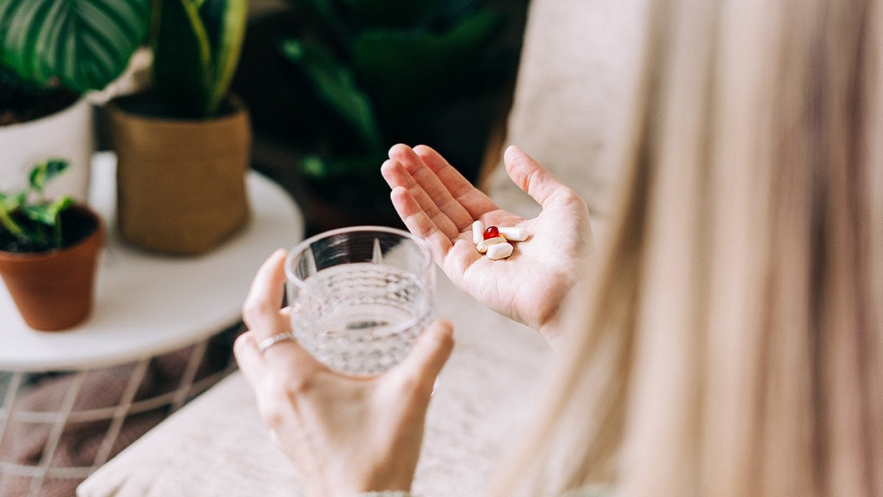 A woman holding multiple pills to drink with a glass of water.