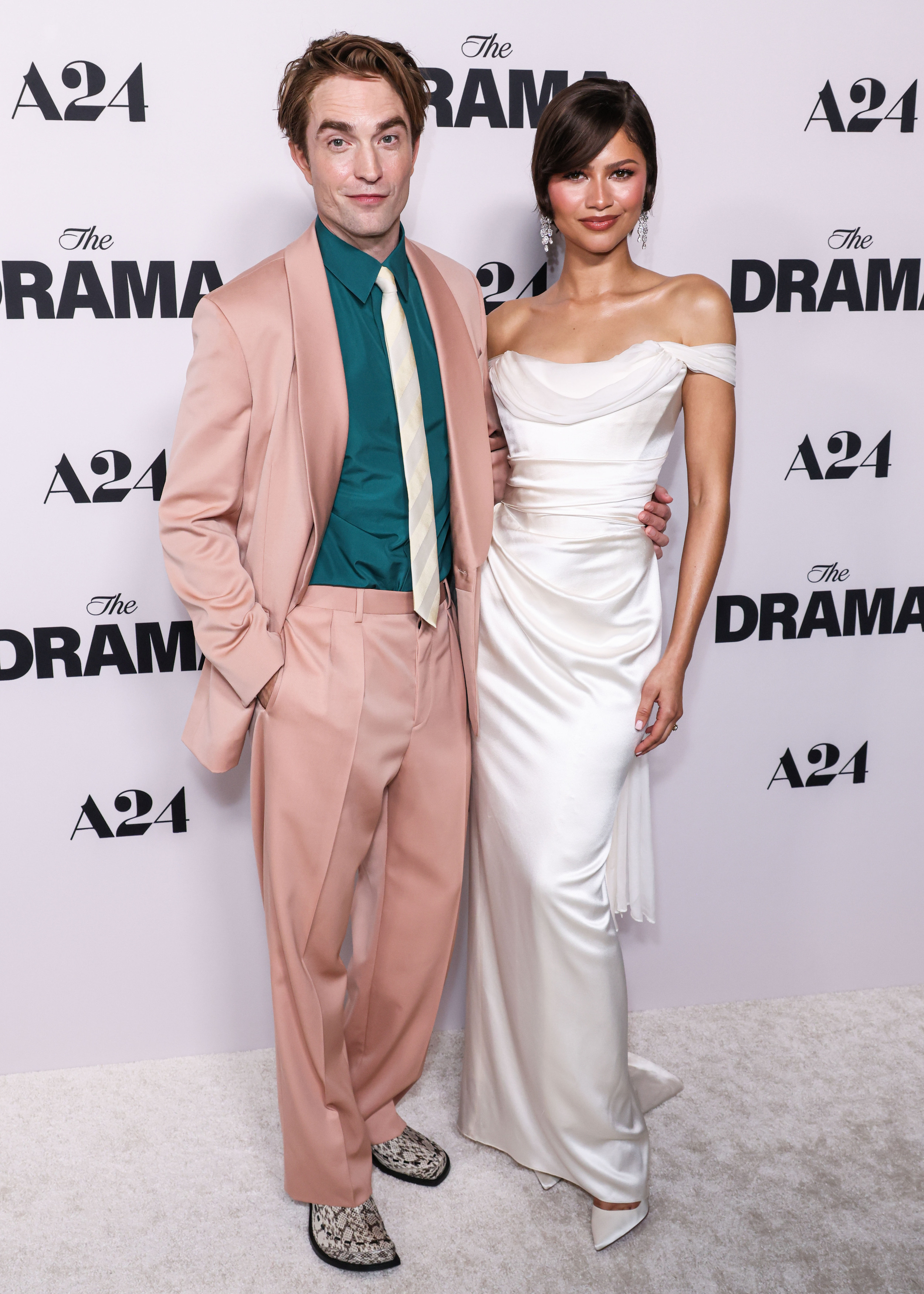Robert Pattinson in a pink suit and Zendaya in a white dress posing at the premiere of "The Drama".