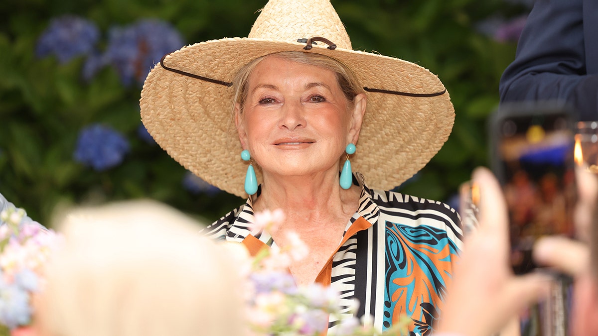 Martha Stewart sitting outside at dinner in Nantucket wearing hanging turquoise earrings and large sunhat.