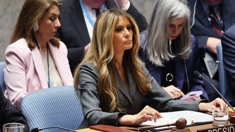 Melania Trump in a grey blazer sitting at a desk