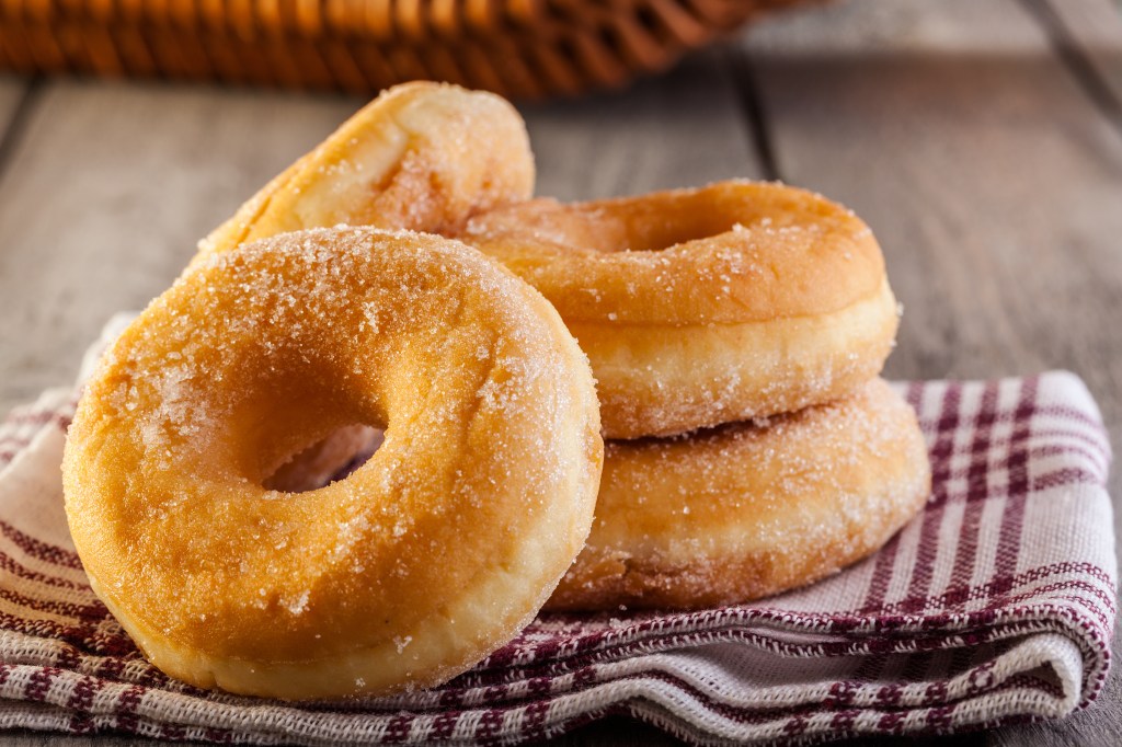 Four sugar-dusted doughnuts on a striped napkin.