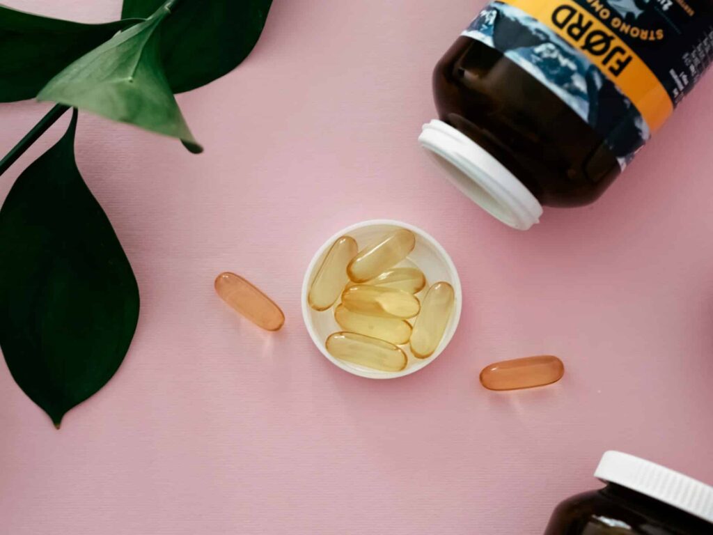 Omega-3 fish oil capsules in a white dish with a supplement bottle on a pink background.