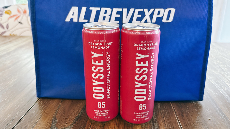 Odyssey cans on wooden table in front of a blue bag from the Alt Bev Expo
