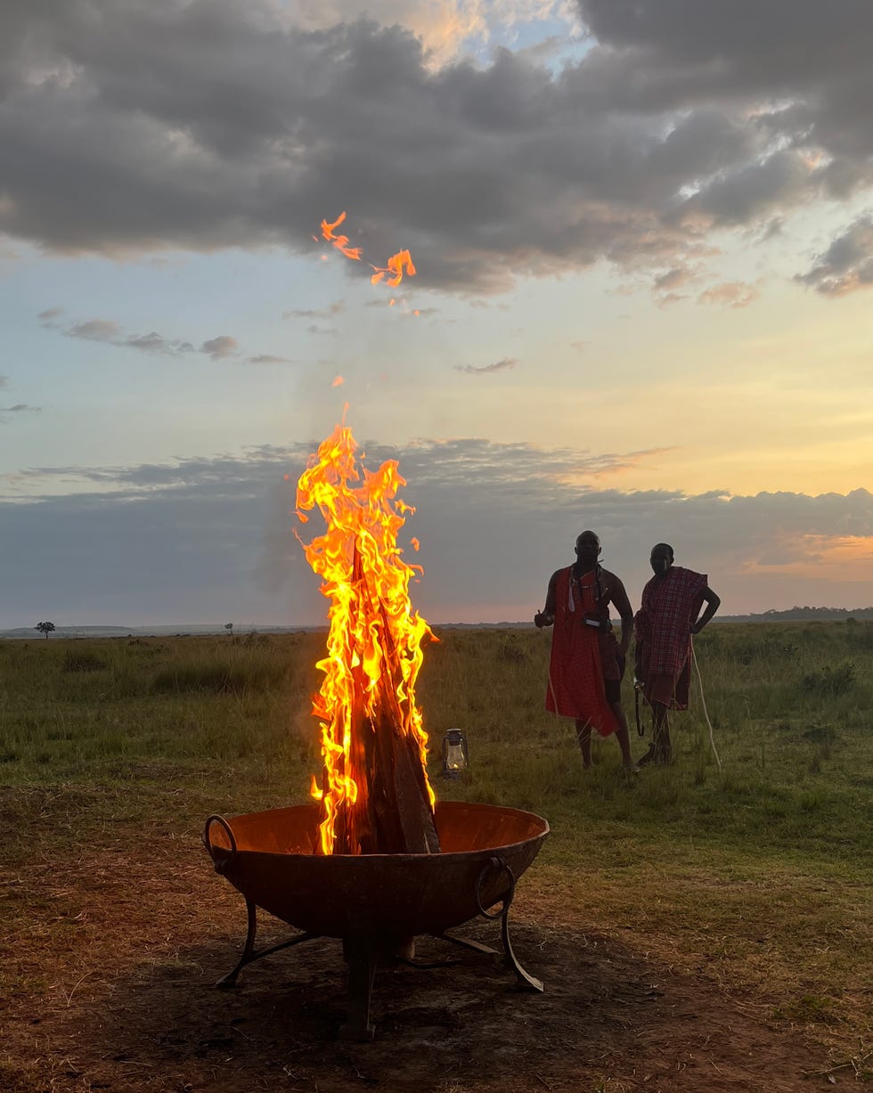 campfire with two figures in the background during sunset paradise plains kenya