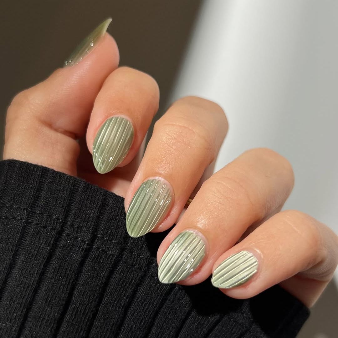 nail design with a textured pattern in soft green against a black ribbed fabric background