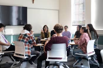 group of students and professor sitting in chairs in a circle while professor lectures