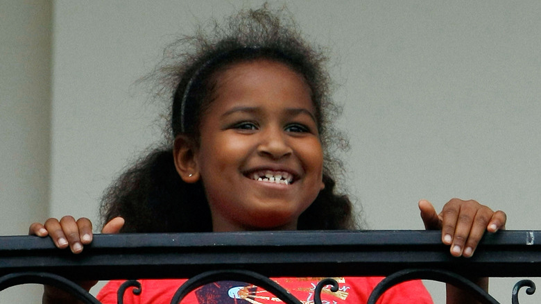 Sasha Obama smiles while holding onto a balcony railing