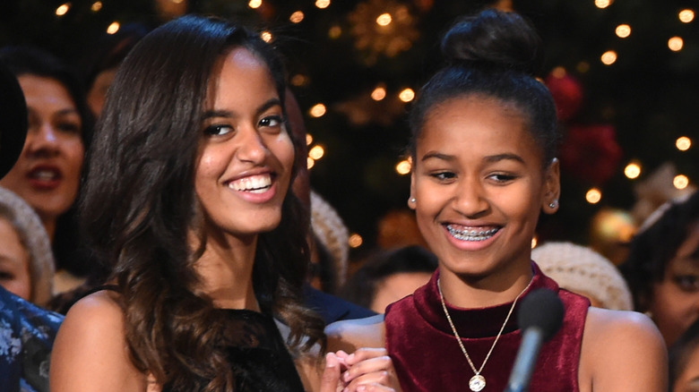Malia Obama smiles next to Sasha Obama behind a microphone