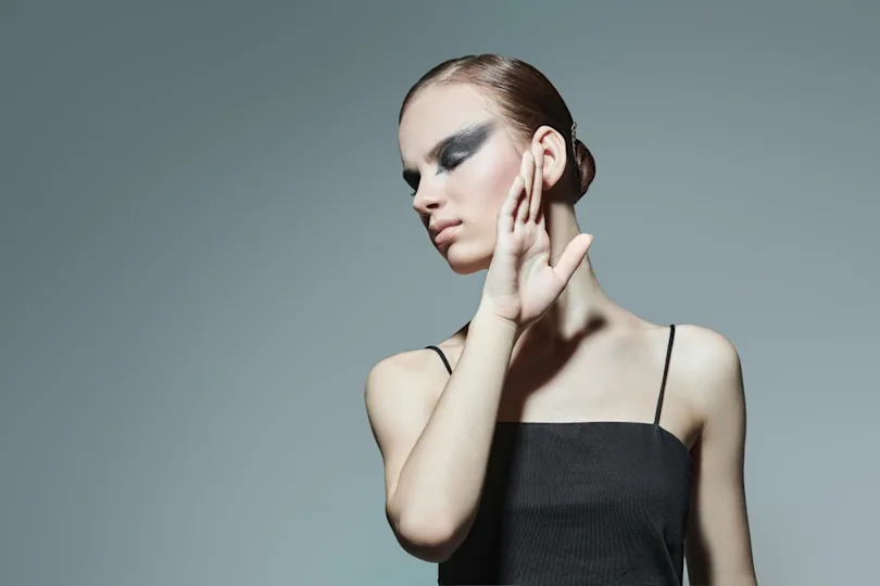 Artistic makeup and hairstyel. Portrait of a beautiful ballerina in dramatic stage makeup. Gray studio background with copy space.