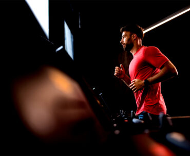 A man wearing a red shirt is running on a treadmill indoors.