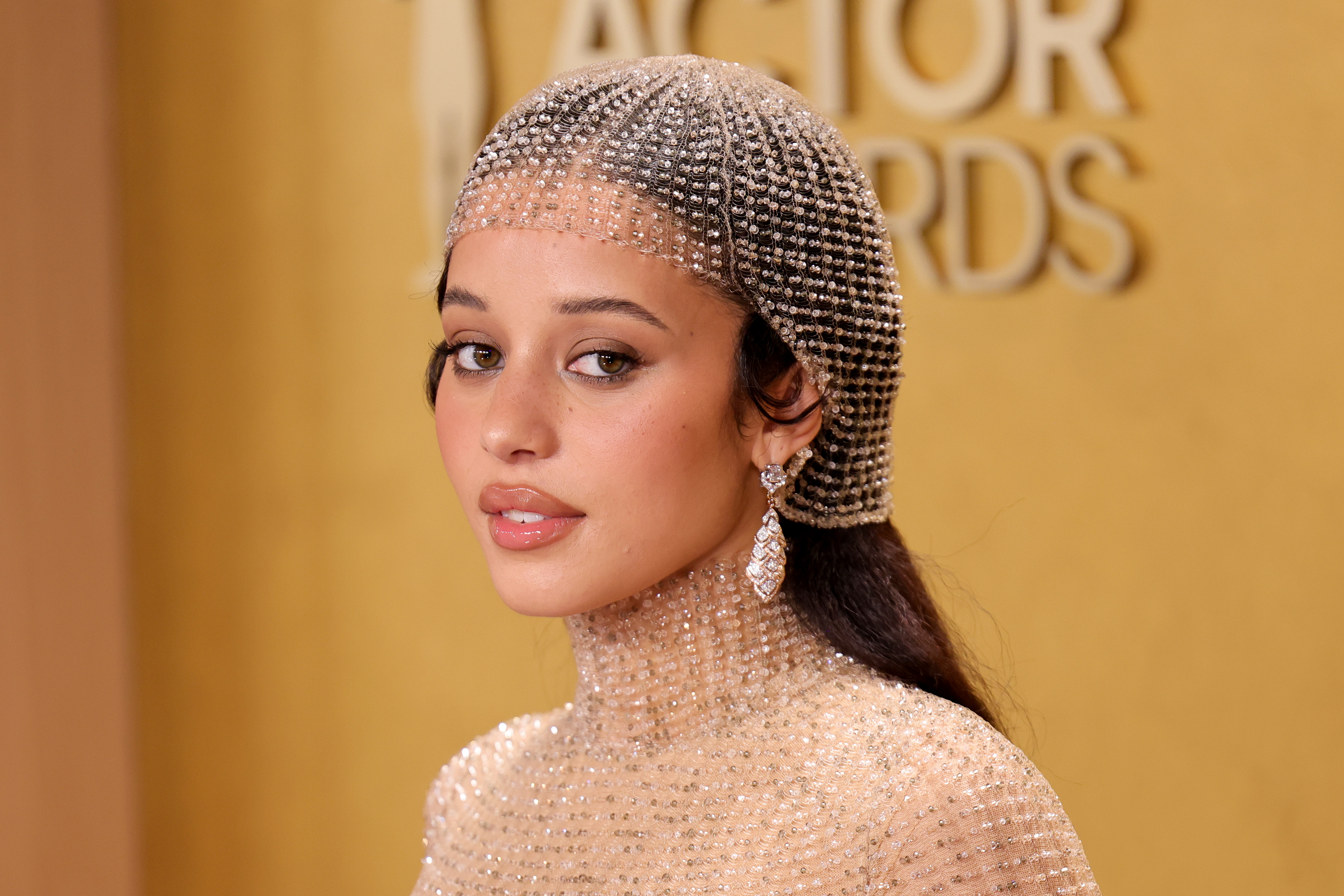 a young woman poses on a red carpet wearing a mesh headpiece