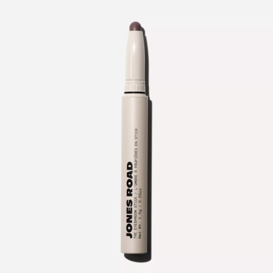 A product shot of the Jones Road Eyeshadow Stick, in a smoky brown shade, on a grey background