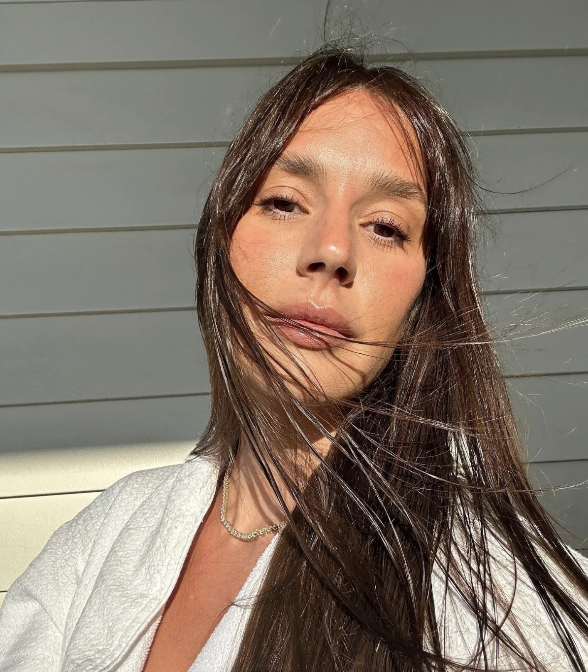 An image of a woman with no makeup on, hair blowing in the breeze.