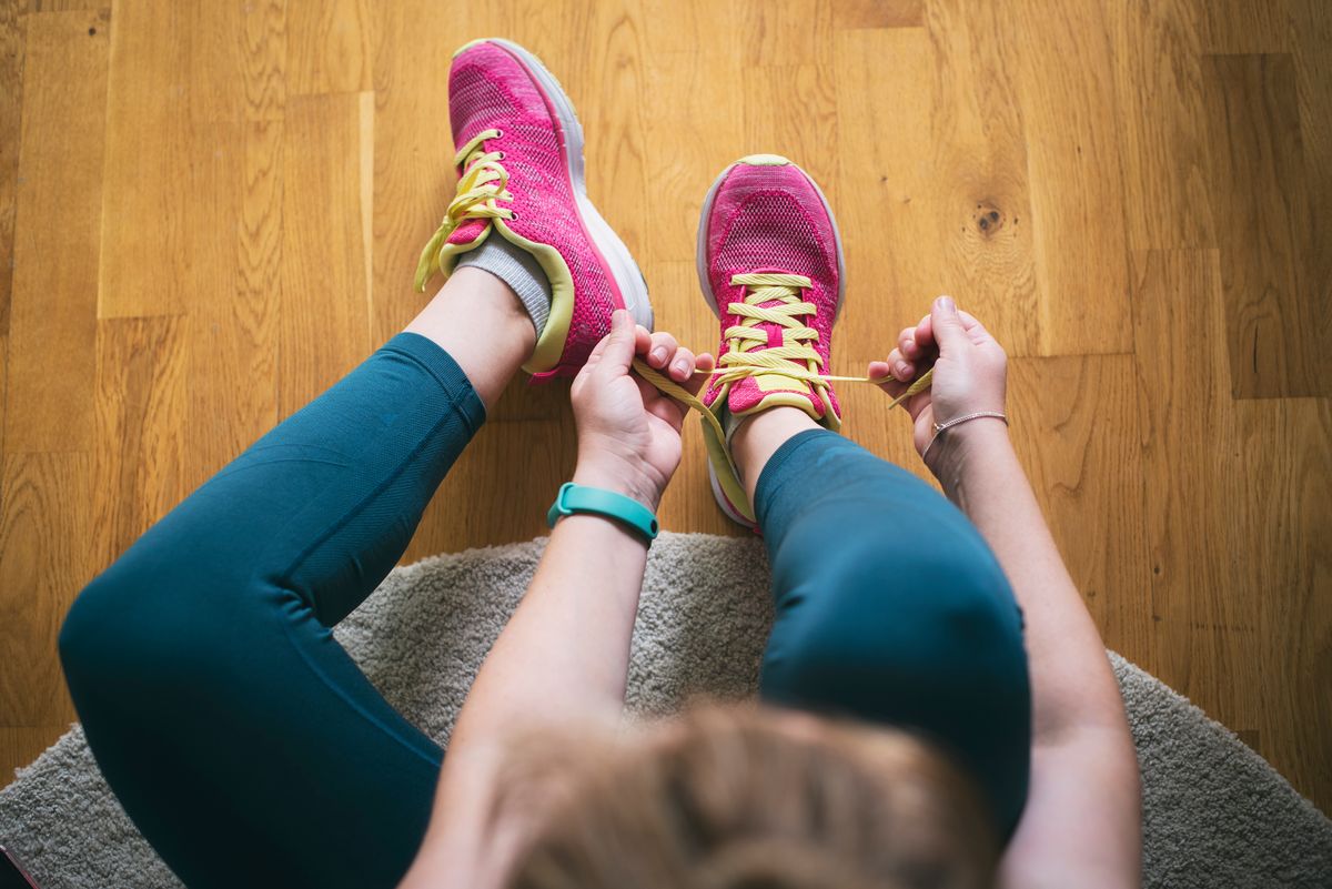 Young sporty woman with smart watch tying shoelaces