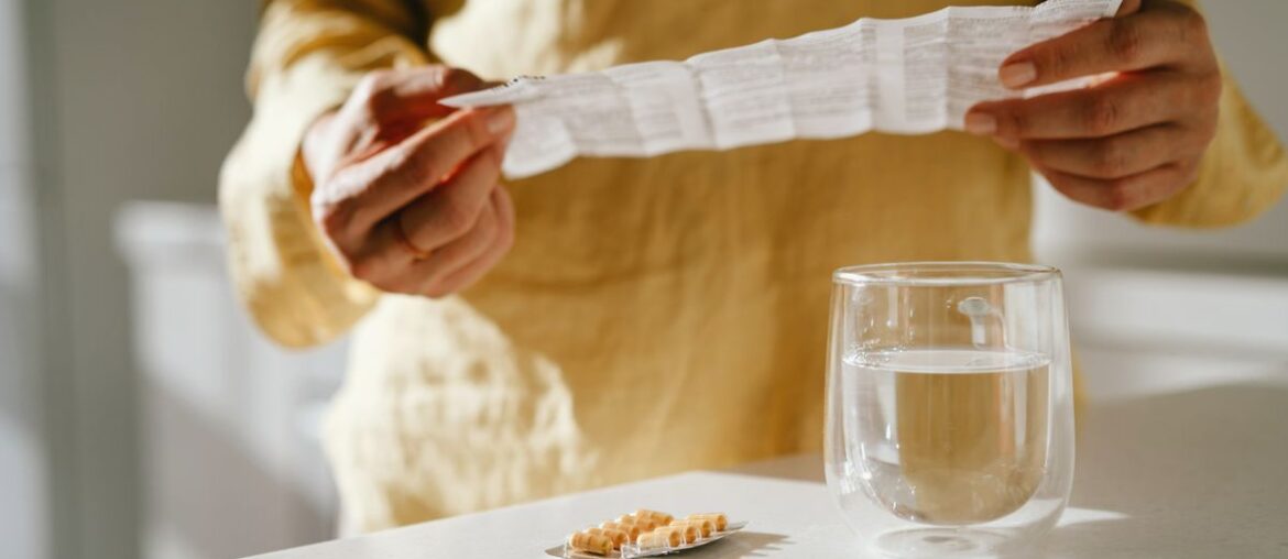 Mature woman standing at a table with green pills in her hand. Taking vitamins, macro elements and bioactive supplements to maintain health. Prevention of colds during an epidemic. The first symptoms of incipient menopause are hypotension or hypertension, hot flashes.