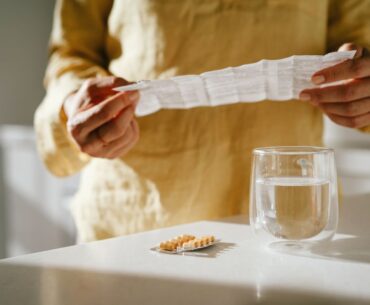 Mature woman standing at a table with green pills in her hand. Taking vitamins, macro elements and bioactive supplements to maintain health. Prevention of colds during an epidemic. The first symptoms of incipient menopause are hypotension or hypertension, hot flashes.