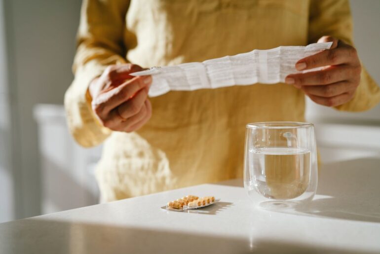 Mature woman standing at a table with green pills in her hand. Taking vitamins, macro elements and bioactive supplements to maintain health. Prevention of colds during an epidemic. The first symptoms of incipient menopause are hypotension or hypertension, hot flashes.