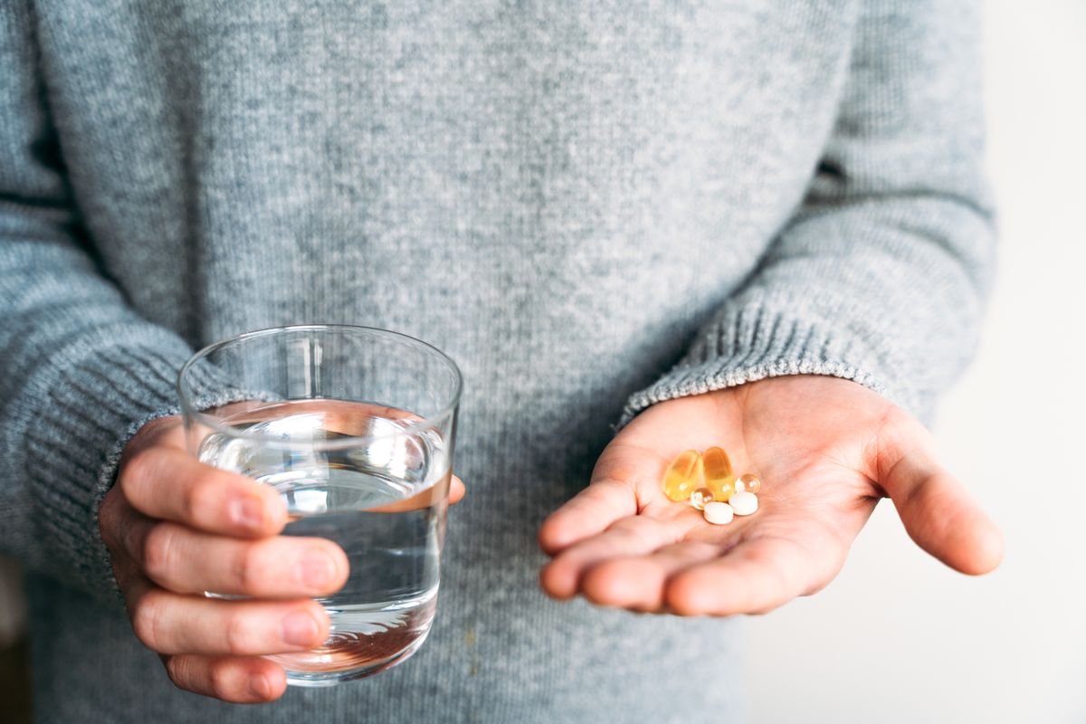 Person holding water and dietary supplements, illustrating a balanced approach to health, hydration and daily self-care in a clean, minimal environment