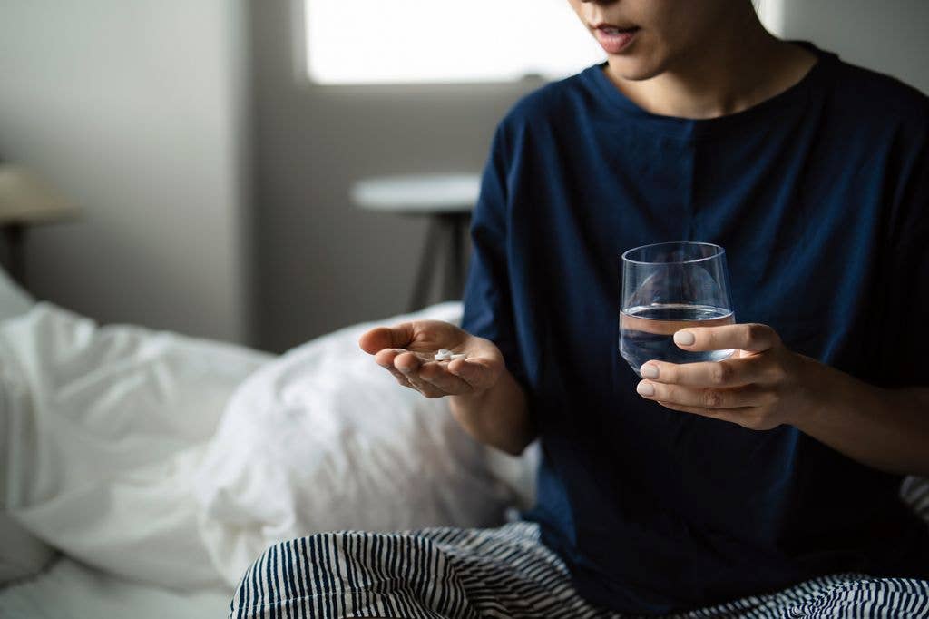 Cropped shot of young Asian woman taking medicines in hand with a glass of water at home. Feeling sick. Medicine, healthcare, supplements and wellbeing concepts